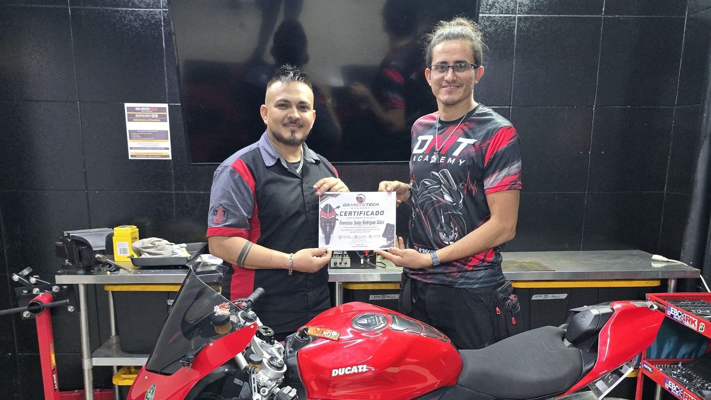 Huberth entrega un certificado a un alumno junto a una Ducati Panigale en el taller
