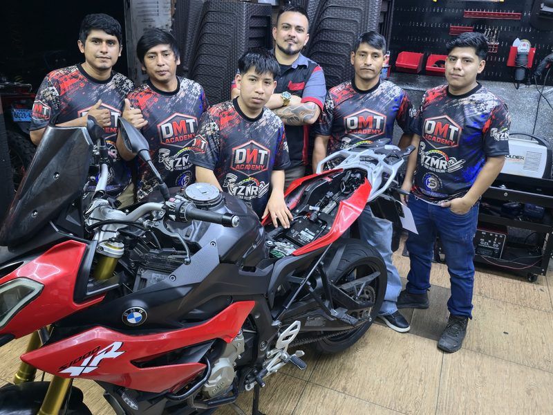 Alumnos con la camiseta DMT Academy junto a una BMW S1000XR en Lima